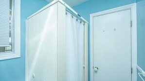 Une salle de bain avec une douche, une porte et une fenêtre équipée de stores.