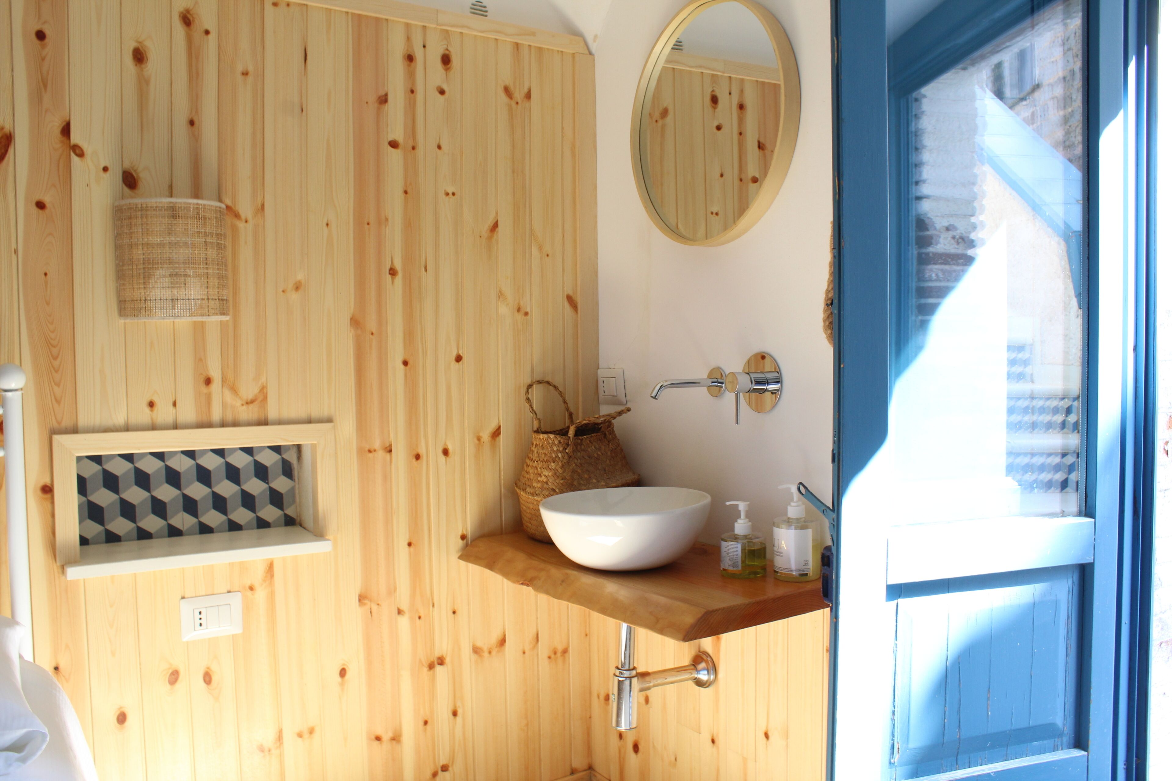 Un baño de madera con lavamanos blanco, un espejo y una repisa con artículos de aseo.