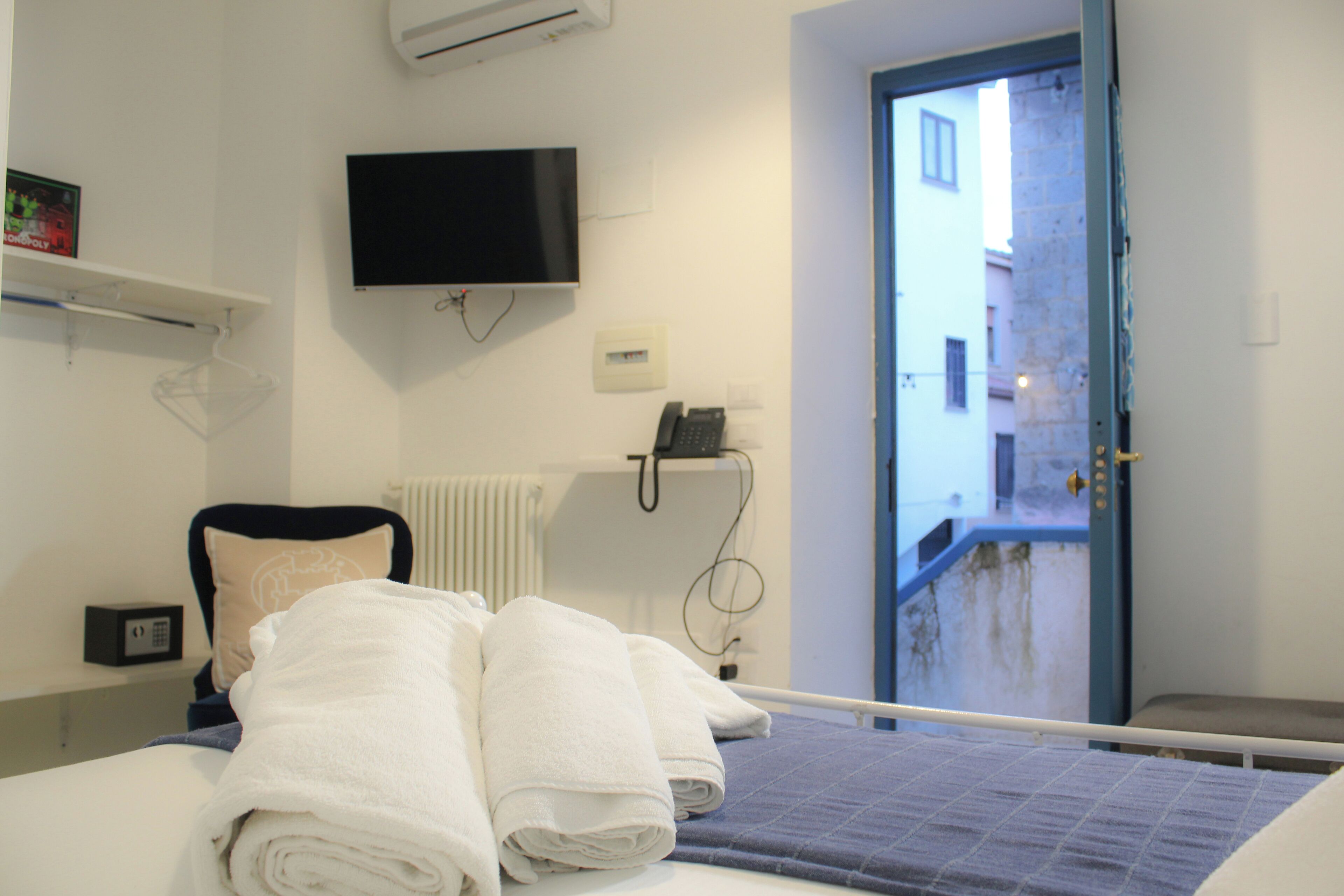 Habitación de hotel con cama, televisor montado en la pared, teléfono junto a la cama y ventana con vista a la calle.
