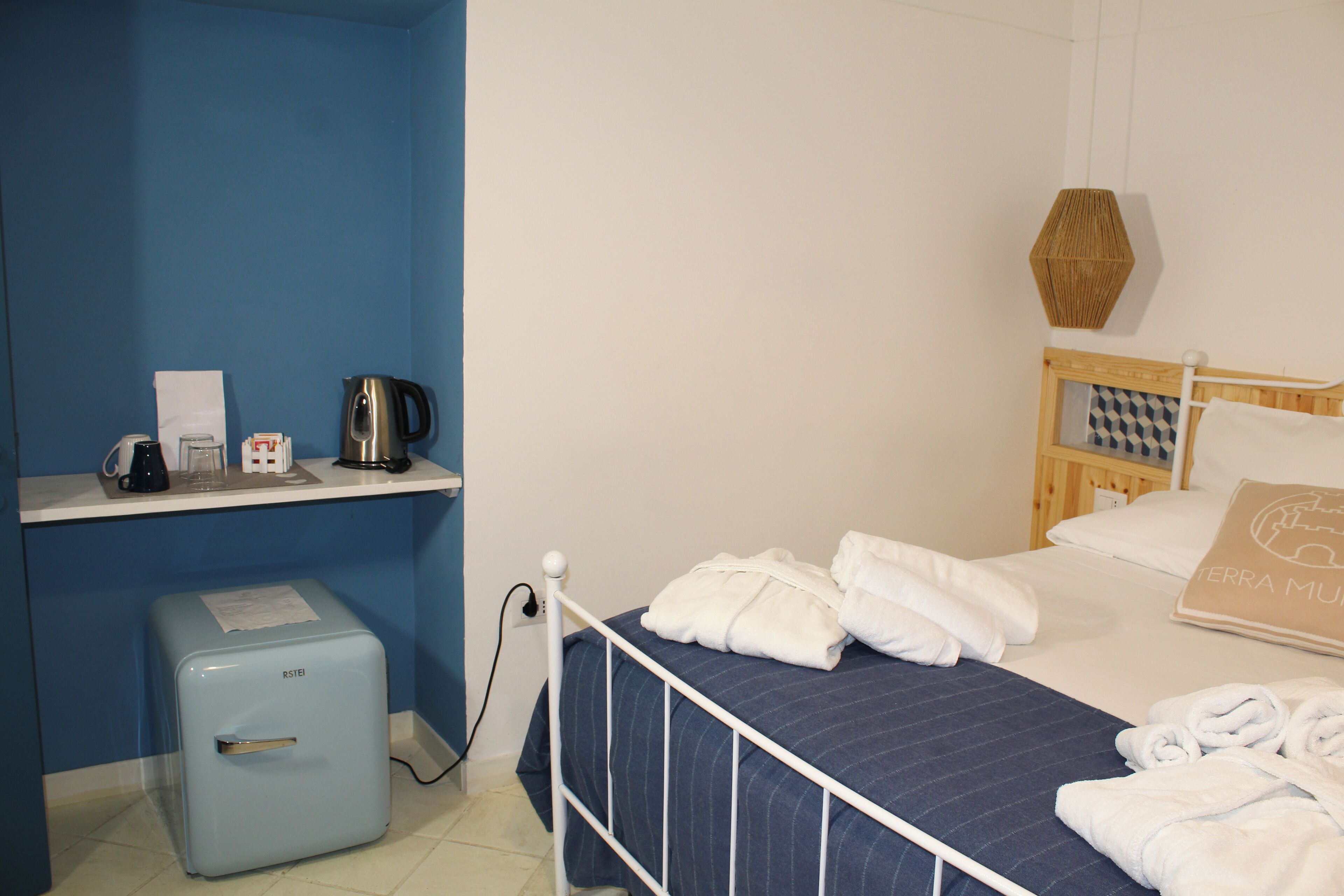 Una habitación de hotel con cama, una kitchenette pequeña, una pared azul y un cabecero de madera.