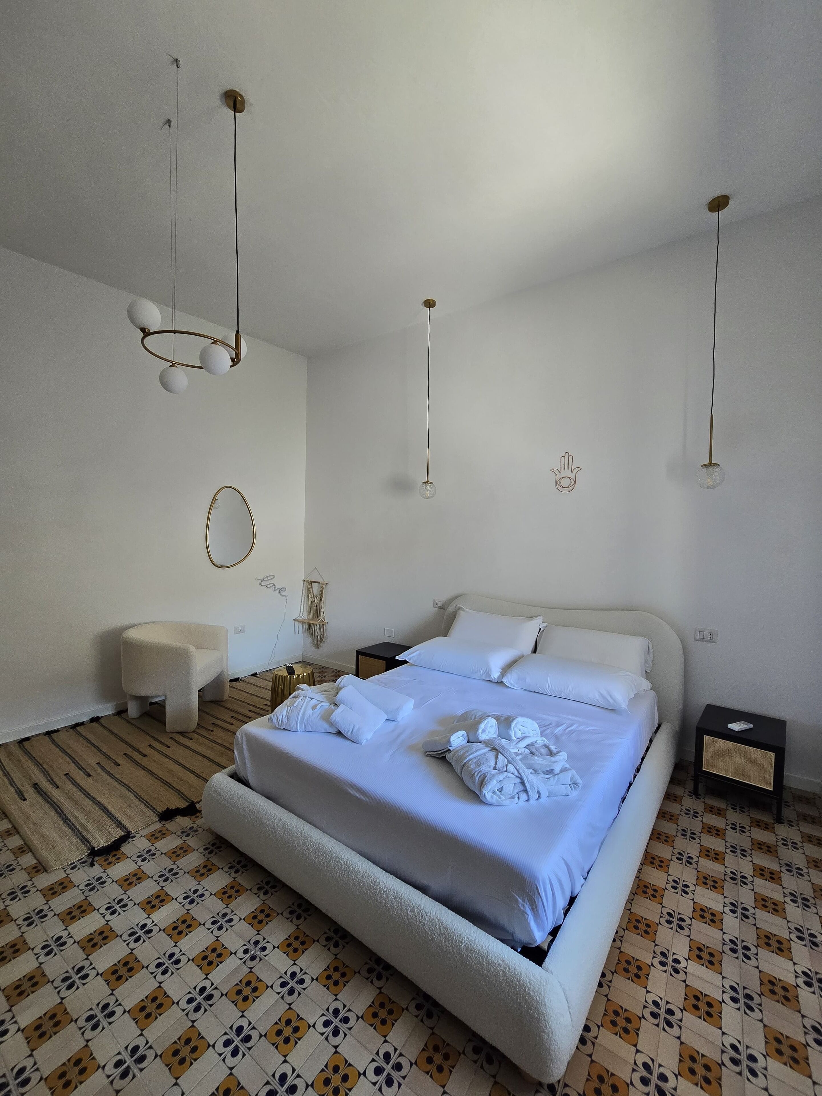 A neatly made bed with white linens, a small bedside table, and a hanging light fixture.