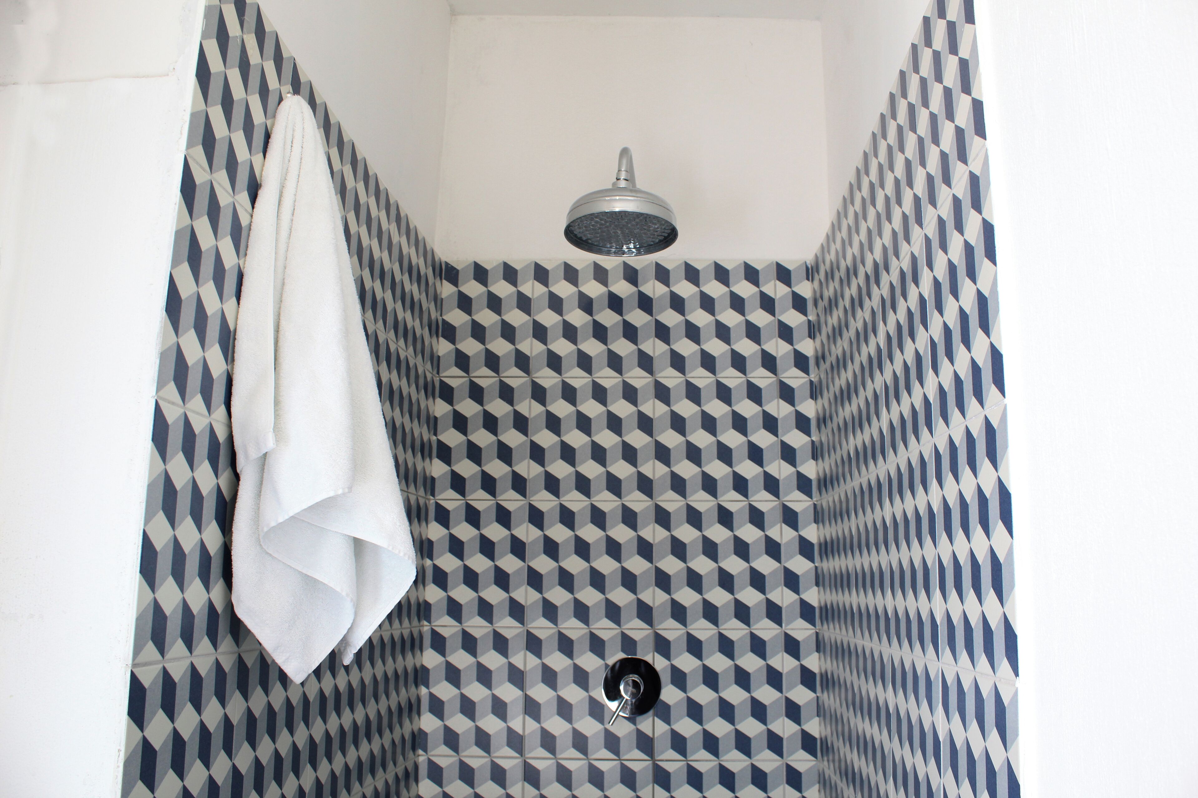 Eine Dusche mit einem geometrischen Fliesenmuster und einem aufgehängten Handtuch.
