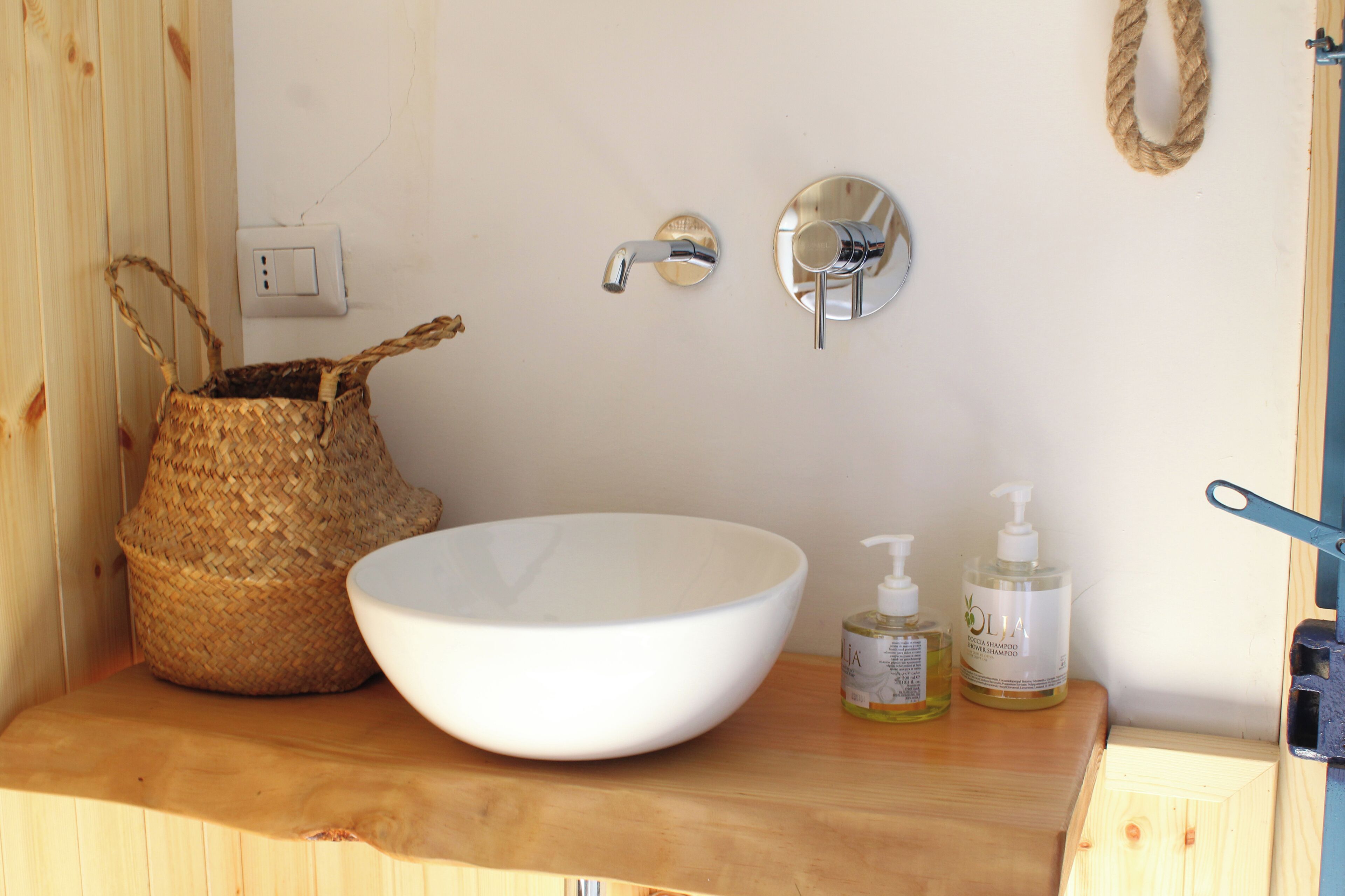 Une coiffeuse en bois avec un lavabo blanc, un panier en osier et deux bouteilles de savon liquide.