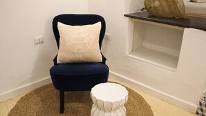 Una sedia con un cuscino, uno sgabello bianco e un tappeto intrecciato in una stanza con pareti bianche e pavimento in legno.