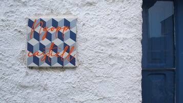 Eine strukturierte weiße Wand mit einer blauen Tür und einem Schild, das in orangefarbener Schreibschrift 'Noop Castle' zeigt.