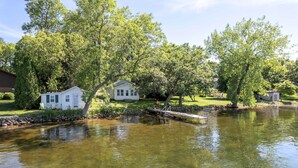 A serene lakeside property with a white house, a dock, and lush greenery. - The Cowdry Cottage | Pet-Friendly | Canoe | Bikes (Alexandria)