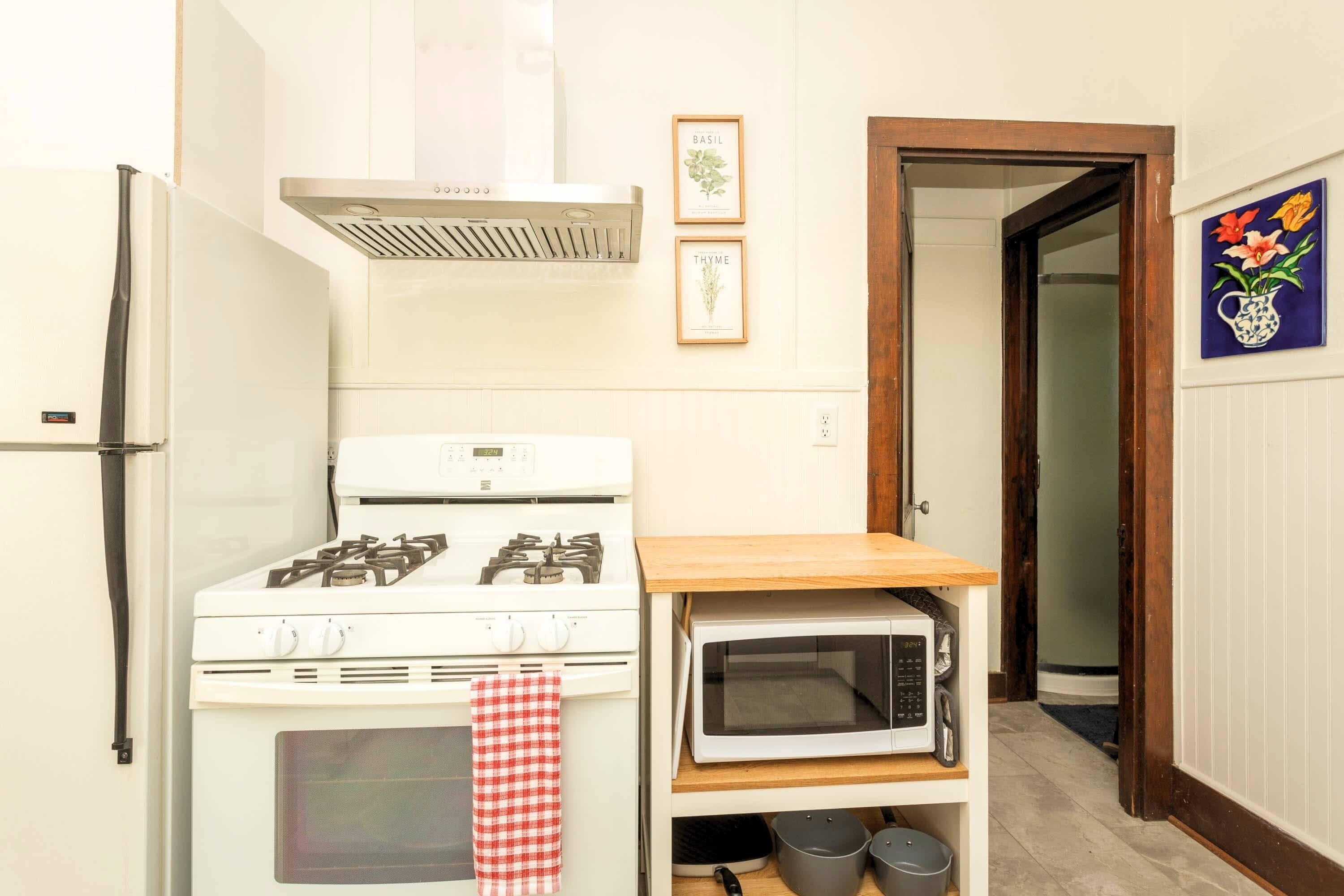 A compact kitchen with a stove, oven, microwave, and a small wooden shelf.