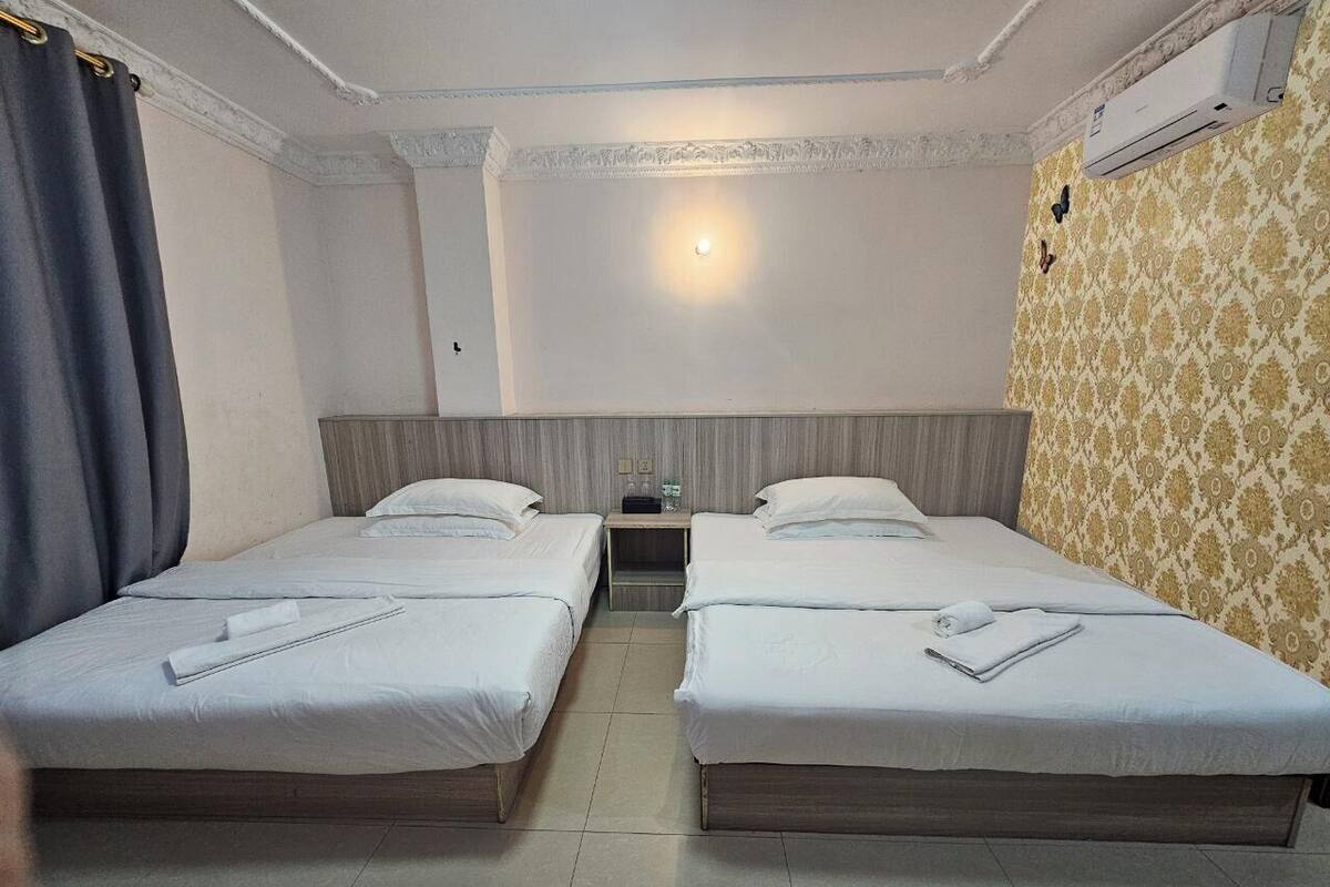 Ein Hotelzimmer mit zwei Einzelbetten, einem Nachttisch, einer Wand-Klimaanlage und einem Wandhintergrund mit Muster.