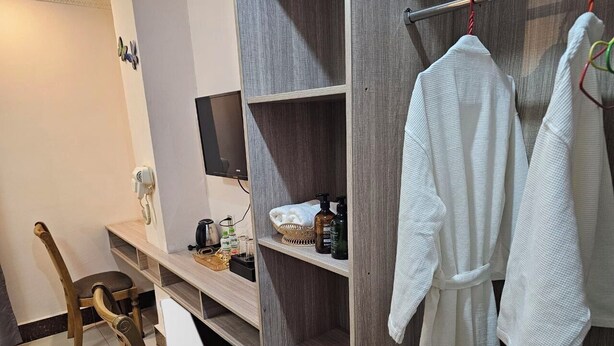 A hotel room with a wooden chair, a desk with a computer, a TV mounted on the wall, and a wardrobe with clothes hanging. - Thon Thean Hotel  (Phnom Penh)