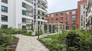 A courtyard with a paved walkway, surrounded by greenery and modern buildings with balconies. - Modern Apartment | Parking, Balcony and Workspace (Gdansk)