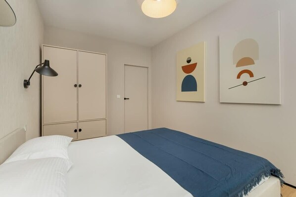 A bedroom with a bed, a wardrobe, a door, and two wall-mounted artworks.