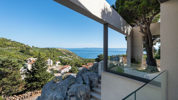 A modern building with a glass balcony overlooking a coastal landscape. - Deluxe apartment Noeli (Krvavica)