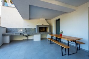 A modern kitchen with a built-in stove, granite countertops, and a wooden dining table with benches. - Deluxe apartment Noeli (Krvavica)