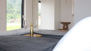 Een kamer met een bed, een tafel met een fles en glazen, en uitzicht op groen buiten.