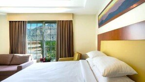 A hotel room with a bed, a sofa, a chair, and a large window with curtains. - Avari Xpress Skardu (Skardu)