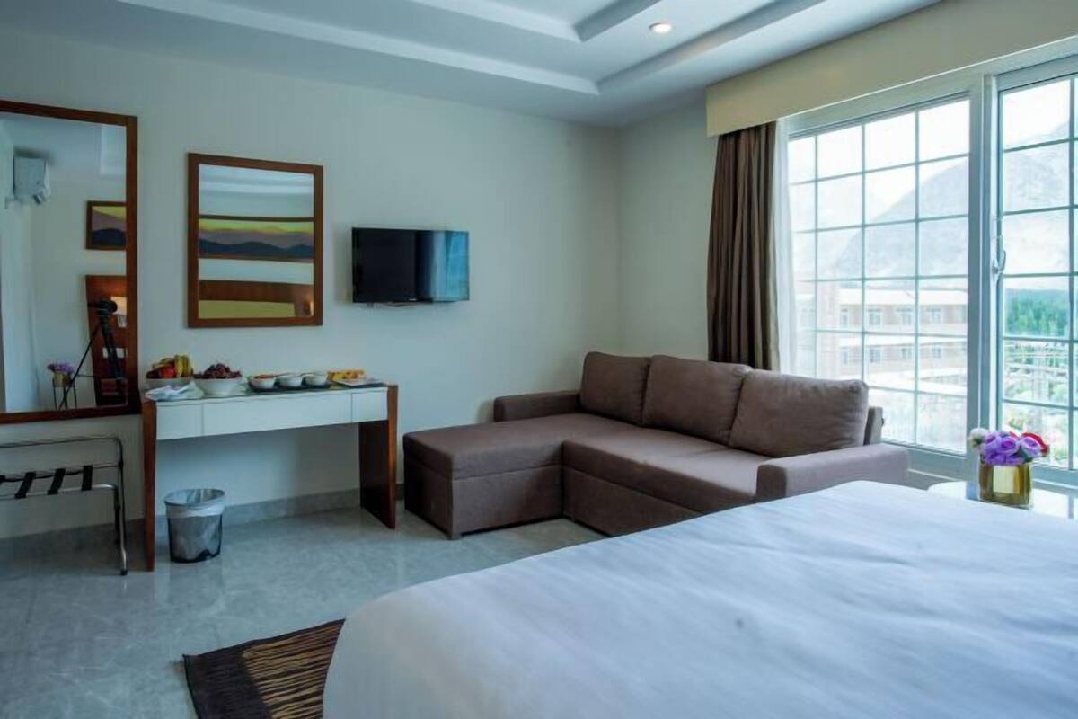 Habitación de hotel con cama, escritorio con televisor, sofá y ventana con vistas.
