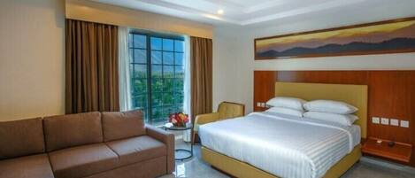 A hotel room with a large bed, a sofa, a small table with flowers, and a window with curtains.