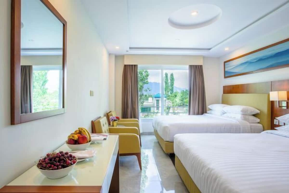 Habitación de hotel con dos camas, un escritorio con fruta, vistas a zonas verdes y montañas, y un cuadro grande en la pared.
