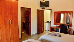 A hotel room with two beds, a desk, a TV, and wooden wardrobes. - Lucca Lodge  (Musina)