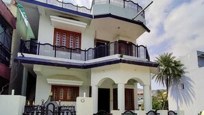 A two-story house with a balcony, a gated entrance, and a parked car.