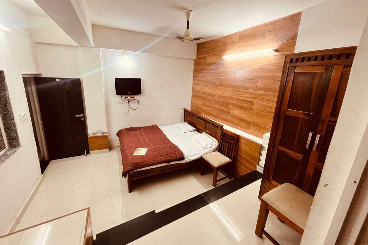 A bedroom with a bed, a TV mounted on the wall, a wardrobe, and a ceiling fan.