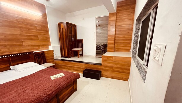 A bedroom with a wooden headboard, a bed with a red bedspread, a wardrobe, a mirror, and a window.