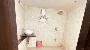 A bathroom with a white sink, a pink bucket, and a marble wall.