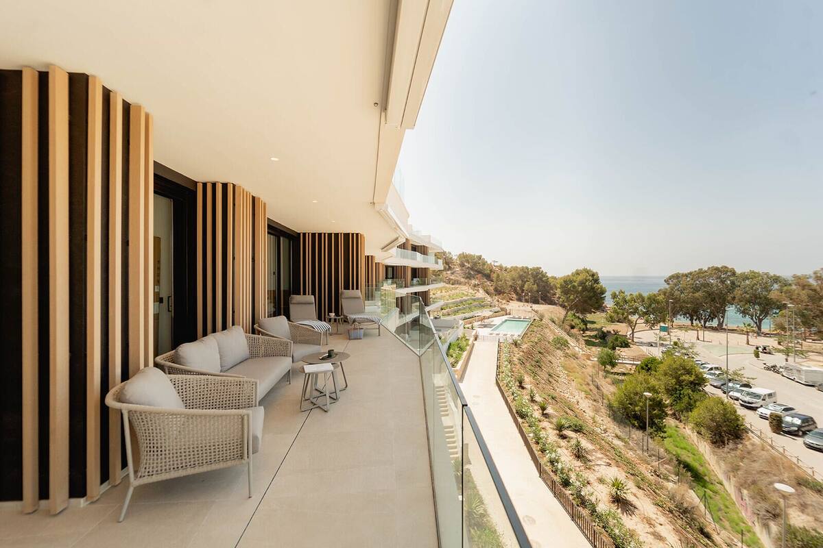 A balcony with wicker furniture, a pool, and a view of the sea.