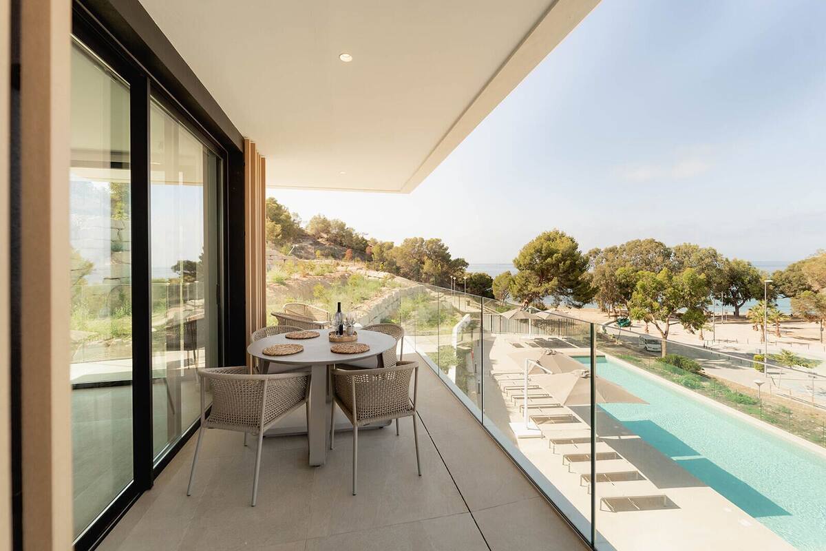 A balcony with a table and chairs overlooking a swimming pool and a scenic view of trees and hills.