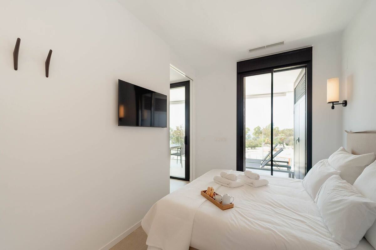 A modern hotel room with a large bed, a flat-screen TV mounted on the wall, and a balcony with a view.