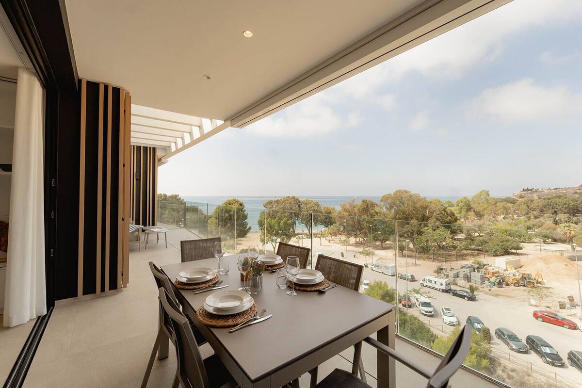 A dining area with a table set for four, overlooking a scenic view of the sea and a construction site.