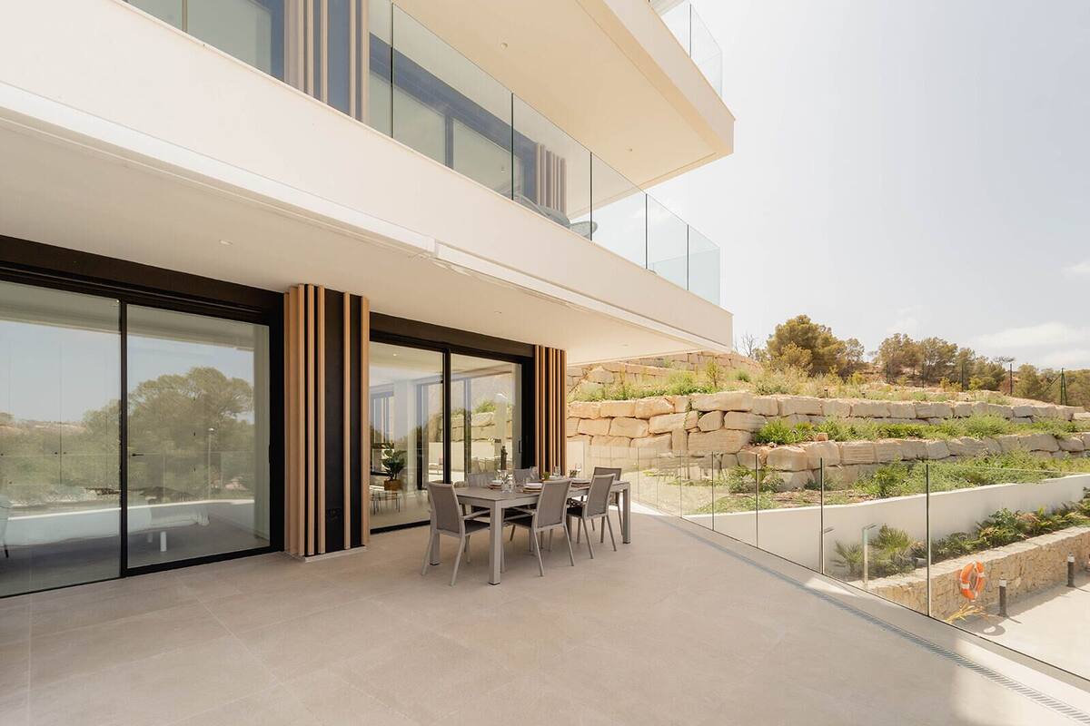 A modern two-story house with a balcony, large glass doors, and a dining area with outdoor furniture.
