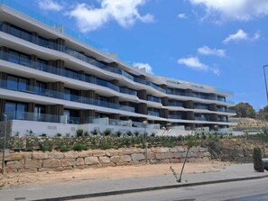 A multi-story hotel with balconies, a stone retaining wall, and a clear sky. - Pure Sea  Apartments (Villajoyosa)