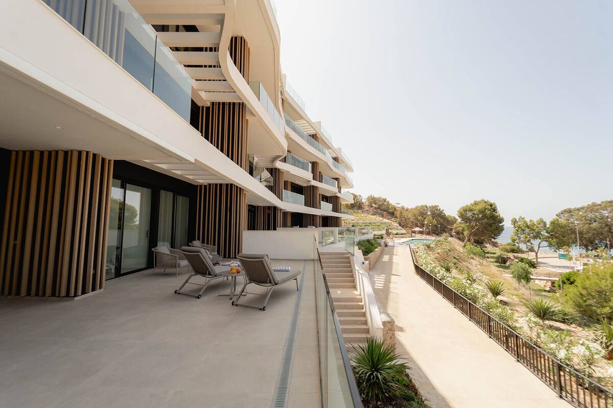 A modern hotel with a curved facade, outdoor seating area with lounge chairs, and a view of the sea.