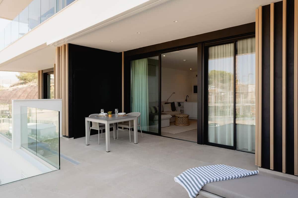 A modern outdoor patio with a dining table and chairs, a cushioned seating area, and a glass balustrade.