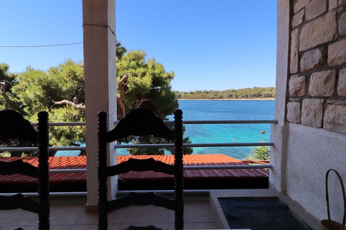 A balcony with a view of a turquoise sea and a forested coastline.