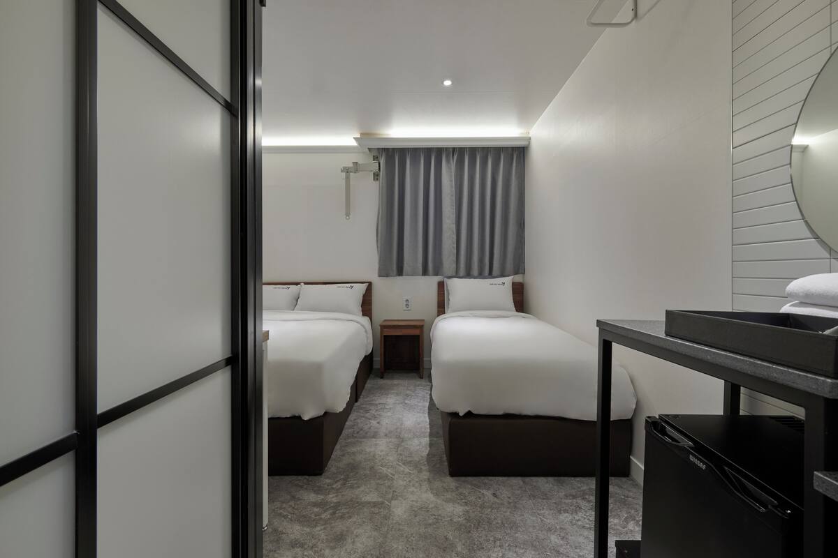 Une chambre d’hôtel avec deux lits, un bureau, un réfrigérateur noir et une fenêtre avec des rideaux.