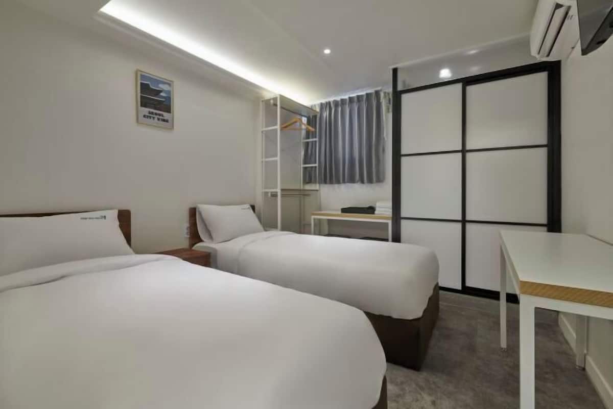 Une chambre d’hôtel avec deux lits, un bureau, une armoire et un espace douche.