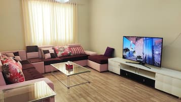 Un salon moderne avec un canapé d’angle, une table basse en verre, un téléviseur à écran plat et un lustre.