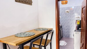 Een eethoek met een houten tafel en twee stoelen, een decoratief bord aan de muur, en een keuken zichtbaar door een open deur.