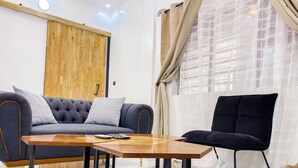 Een moderne woonkamer met een grijze bank, een zwarte fauteuil en een houten salontafel.