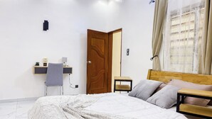Een slaapkamer met een groot bed, een houten hoofdbord, een nachtkastje, een stoel, een klein bureau met lamp en een wandluidspreker.