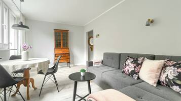 En moderne stue med en grå sofa, blomstrede puder, et lille rundt bord og et træskab.