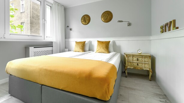 A bedroom with a bed, a nightstand, a window, and a wall-mounted clock. - MARGI Kai Apartament (Szczecin)