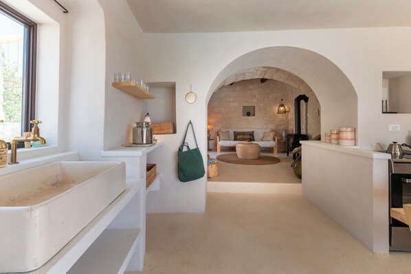 A modern kitchen with a central island, a rustic stone wall, and a view into a cozy living area.