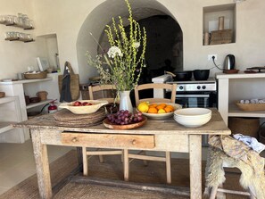 Uma cozinha rústica com uma mesa de madeira, um vaso com flores e diversas tigelas com frutas e vegetais.