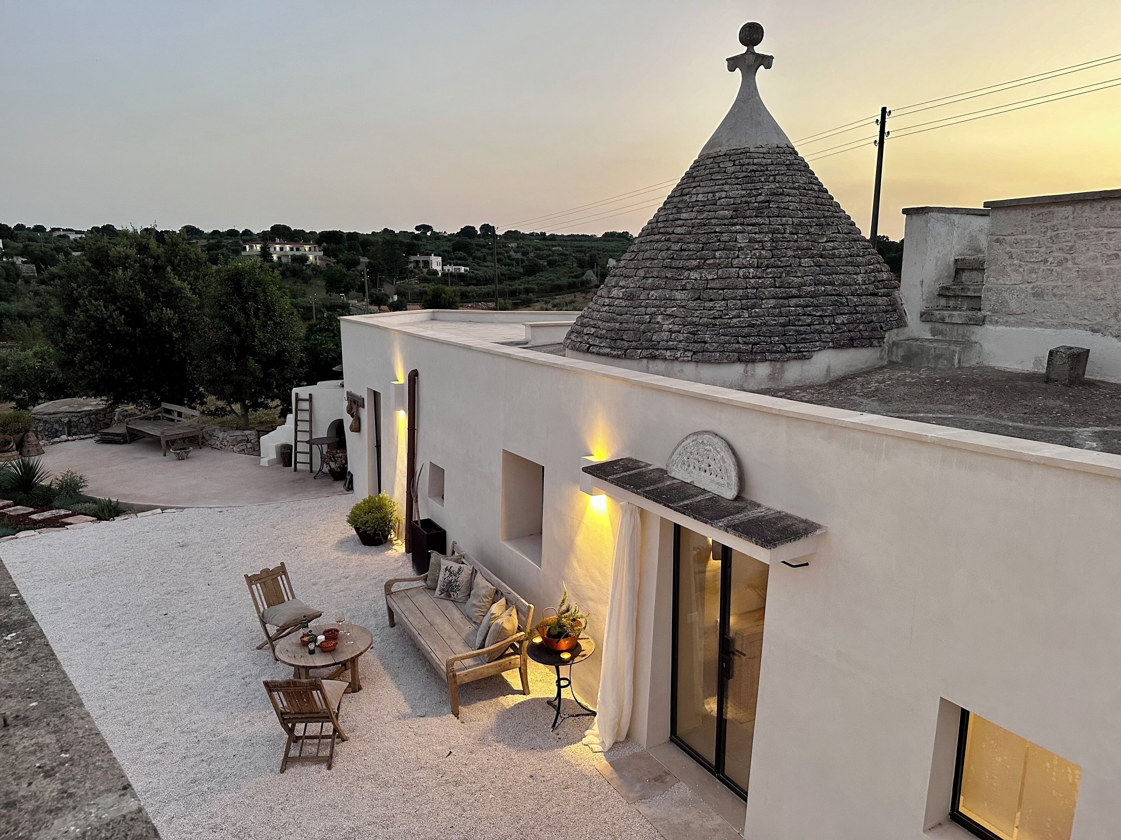 Una villa moderna con tejado de piedra, un espacio exterior acogedor con sofá y sillones, y un pequeño jardín.