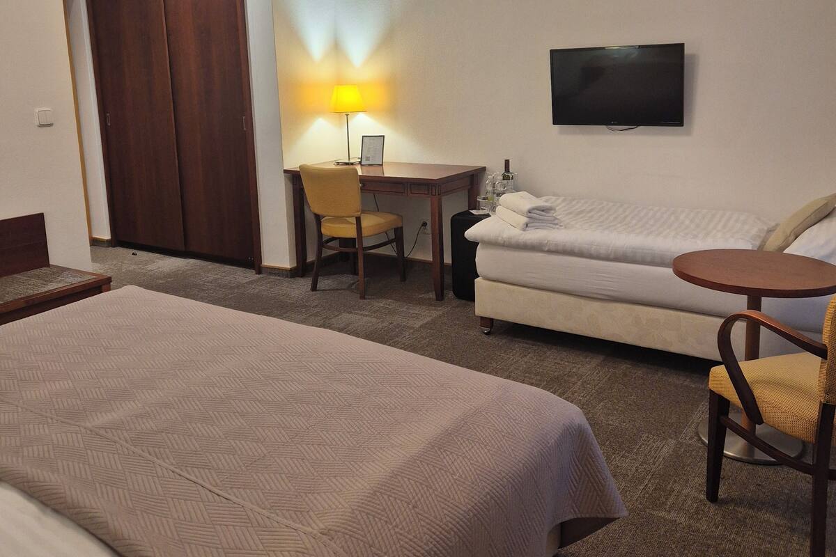 Une chambre d’hôtel avec deux lits, un bureau avec une chaise, un canapé, un téléviseur fixé au mur et une lampe.