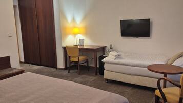Ein Hotelzimmer mit zwei Betten, einem Schreibtisch mit Stuhl, einer Sitzecke und einem Fernseher an der Wand sowie einer Lampe.