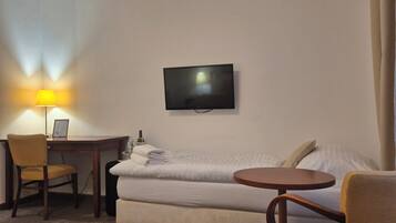 A hotel room with a bed, a desk with a chair, a TV mounted on the wall, and a small round table.